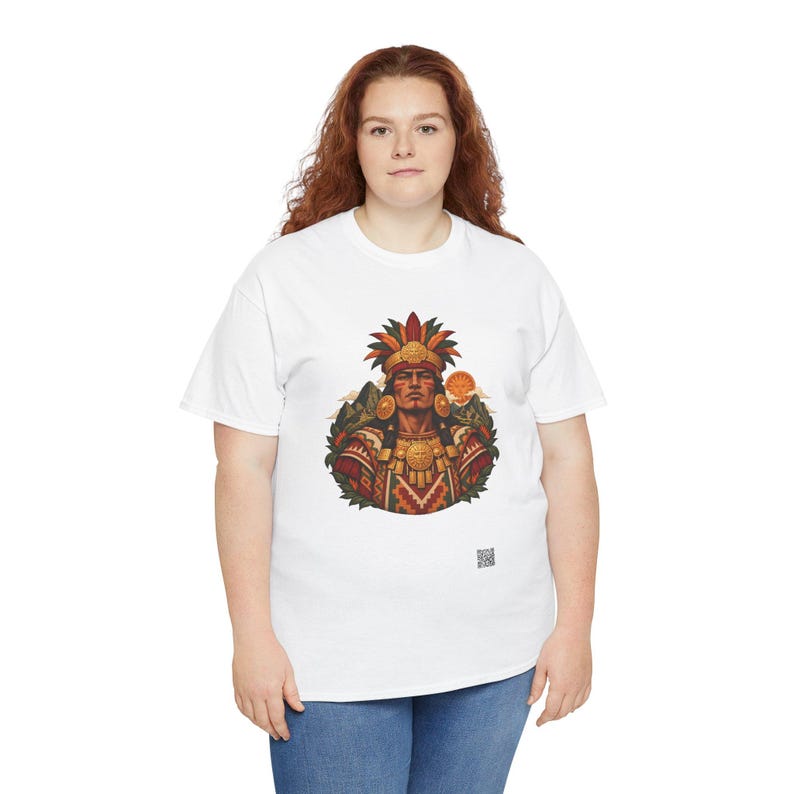 May include: A white short-sleeved t-shirt featuring a central graphic of a person wearing an elaborate feathered headdress and traditional patterned clothing, with a small QR code printed near the bottom right of the design.