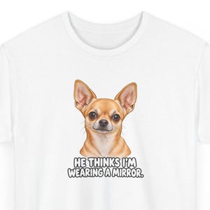 May include: A white t-shirt featuring a graphic illustration of a tan Chihuahua dog with large ears and dark eyes. Below the dog, the text reads: HE THINKS I'M WEARING A MIRROR. The design is centered on the chest of the short-sleeved garment.