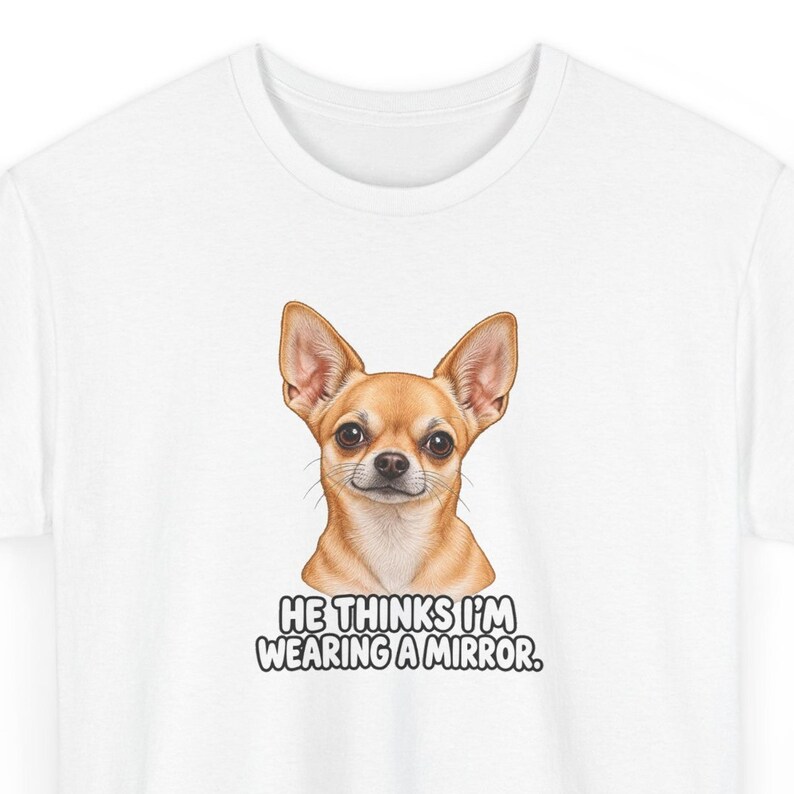May include: A white t-shirt featuring a graphic illustration of a tan Chihuahua dog with large ears and dark eyes. Below the dog, the text reads: HE THINKS I'M WEARING A MIRROR. The design is centered on the chest of the short-sleeved garment.