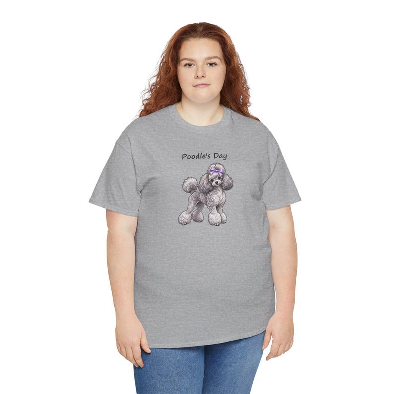 May include: A heather gray short-sleeve t-shirt featuring a graphic of a gray poodle with a purple bow on its head. Above the poodle, the text Poodle's Day is printed in a simple black font. The shirt has a crew neckline and a standard fit.