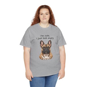 May include: A heather gray short-sleeve t-shirt featuring a graphic of a brown and black French Bulldog. Above the dog, the text reads, "I'm cute, I just look angry" in a simple black font. The shirt has a crew neckline and a standard fit.
