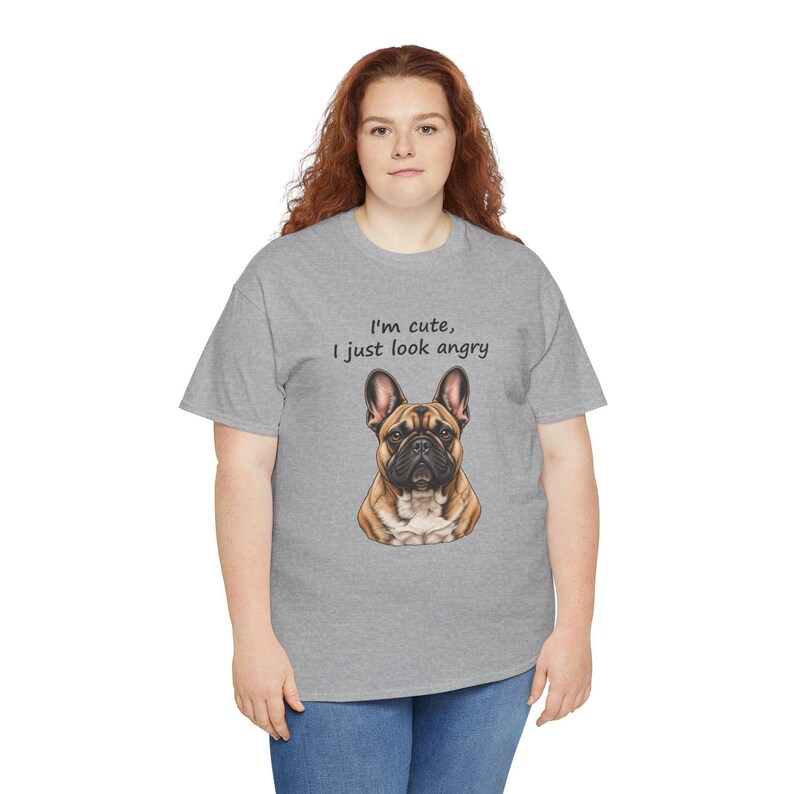 May include: A heather gray short-sleeve t-shirt featuring a graphic of a brown and black French Bulldog. Above the dog, the text reads, "I'm cute, I just look angry" in a simple black font. The shirt has a crew neckline and a standard fit.