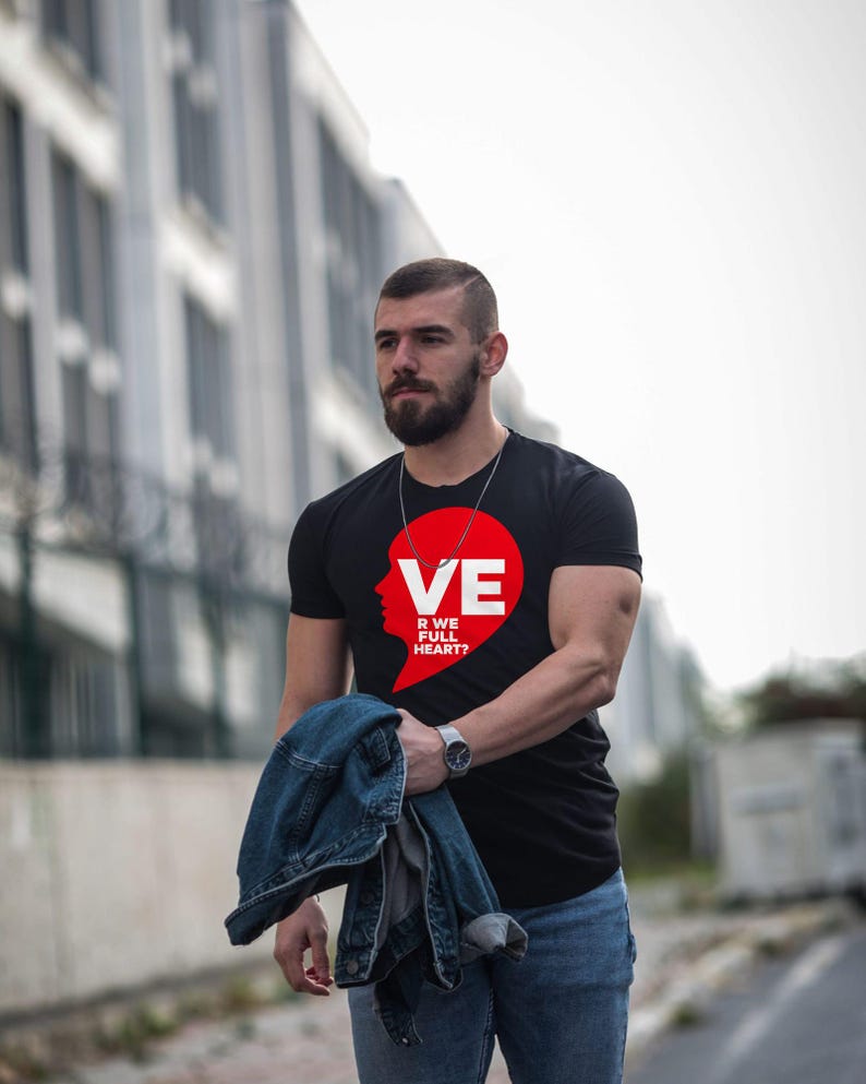 Puede incluir: Una camiseta negra de manga corta con un gr&aacute;fico rojo en forma de coraz&oacute;n en el pecho. El gr&aacute;fico incluye una silueta blanca de un perfil y el texto VE R WE FULL HEART? La camiseta se combina con unos vaqueros azules y una chaqueta vaquera.