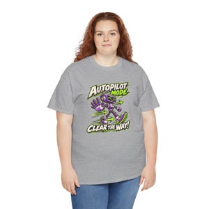 May include: A heather gray short-sleeve t-shirt featuring a graphic of a purple robot walking with one hand raised. The text reads AUTOPILOT MODE and CLEAR THE WAY in bold white and green lettering with green directional arrows.