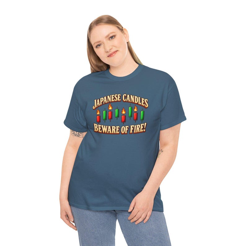 May include: A slate blue short-sleeve t-shirt featuring a graphic of red and green Japanese candlestick chart patterns with flames on top. The text reads JAPANESE CANDLES BEWARE OF FIRE in a bold, stylised font above and below the candles.