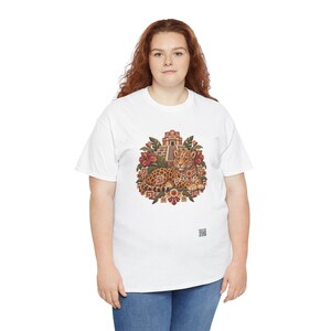 May include: A white short-sleeve t-shirt featuring a central graphic of a spotted jaguar resting in front of a stepped pyramid, surrounded by red hibiscus flowers and green leaves, with geometric patterns and a small QR code at the bottom.