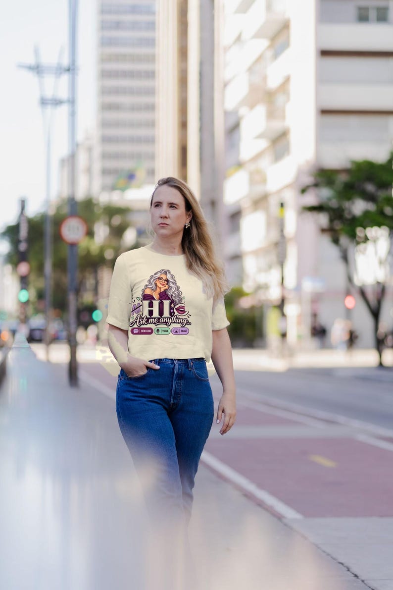 May include: A cream-colored short-sleeve t-shirt featuring a graphic of a woman with long gray hair, the text "HI Ask me anything...", and small icons for new chat, voice, and image, paired with blue denim jeans.