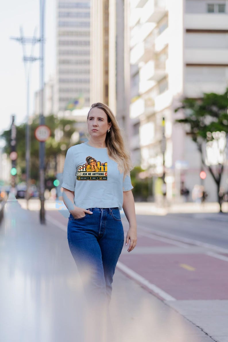 Puede incluir: Una camiseta de manga corta de color azul claro con un estampado gr&aacute;fico de una persona con gafas y el texto "ai hi" y "ASK ME ANYTHING" con iconos y texto m&aacute;s peque&ntilde;os debajo del gr&aacute;fico principal.