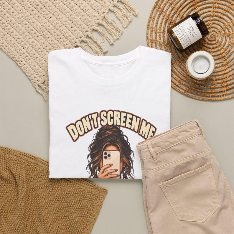 K&ouml;nnte beinhalten: Ein wei&szlig;es T-Shirt mit einer Grafik einer Person mit langem braunen Haar in einem unordentlichen Dutt, die ein Smartphone vor das Gesicht h&auml;lt. &Uuml;ber der Illustration steht der Text "DON'T SCREEN ME" in einer geschwungenen Schrift.