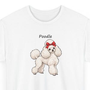 May include: A white t-shirt featuring a graphic illustration of a fluffy white poodle dog with a bright red bow on its head. The word Poodle is printed in black text above the dog. The design is centered on the front of the garment.