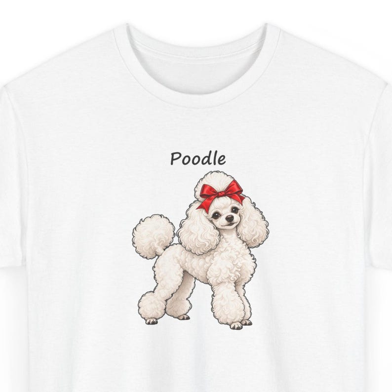 May include: A white t-shirt featuring a graphic illustration of a fluffy white poodle dog with a bright red bow on its head. The word Poodle is printed in black text above the dog. The design is centered on the front of the garment.