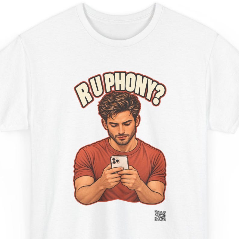 May include: A white t-shirt featuring a graphic illustration of a person with brown hair wearing a red t-shirt and looking down at a smartphone. Above the figure, the text reads RU PHONY? in a bold, arched font. A small QR code is at the bottom.