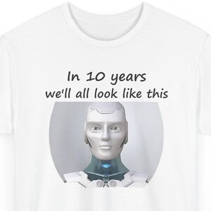 May include: A white t-shirt featuring a graphic of a silver and white humanoid robot head and shoulders. Above the robot, the text reads, In 10 years we'll all look like this, printed in a simple black sans-serif font on the front of the shirt.