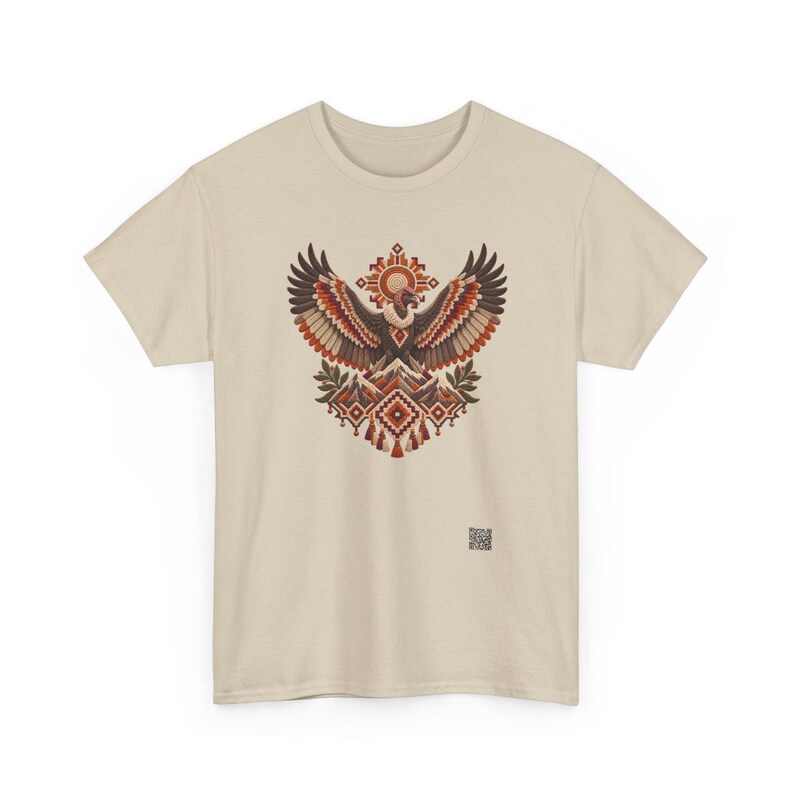 May include: A beige short-sleeve t-shirt featuring a central graphic of a vulture with outstretched wings above a mountain range, accented by geometric patterns in shades of red, brown, and cream, with a small QR code printed near the bottom right.