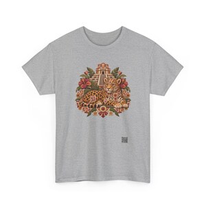 May include: A heather gray t-shirt featuring a central graphic of a spotted jaguar resting in front of a stepped pyramid. The design includes red hibiscus flowers, green leaves, and geometric patterns in shades of orange, brown, and gold.