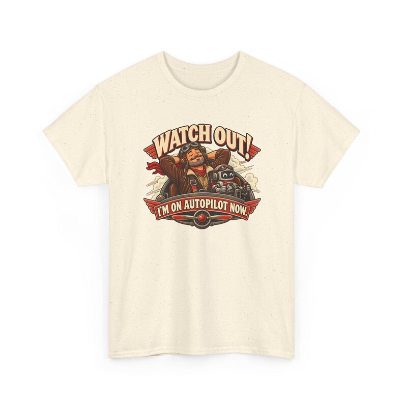 May include: A cream-colored t-shirt featuring a graphic of a pilot and a robot in a cockpit. The text reads WATCH OUT! I'M ON AUTOPILOT NOW. The design includes red wings, a propeller, and clouds in a brown, red, and white color palette.
