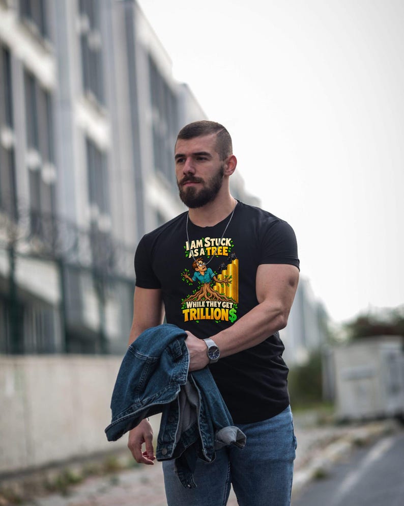 May include: A black short-sleeved t-shirt featuring a graphic of a person transforming into a tree with roots, alongside a rising yellow bar chart. The text reads: I AM STUCK AS A TREE WHILE THEY GET TRILLIONS, with a green dollar sign.