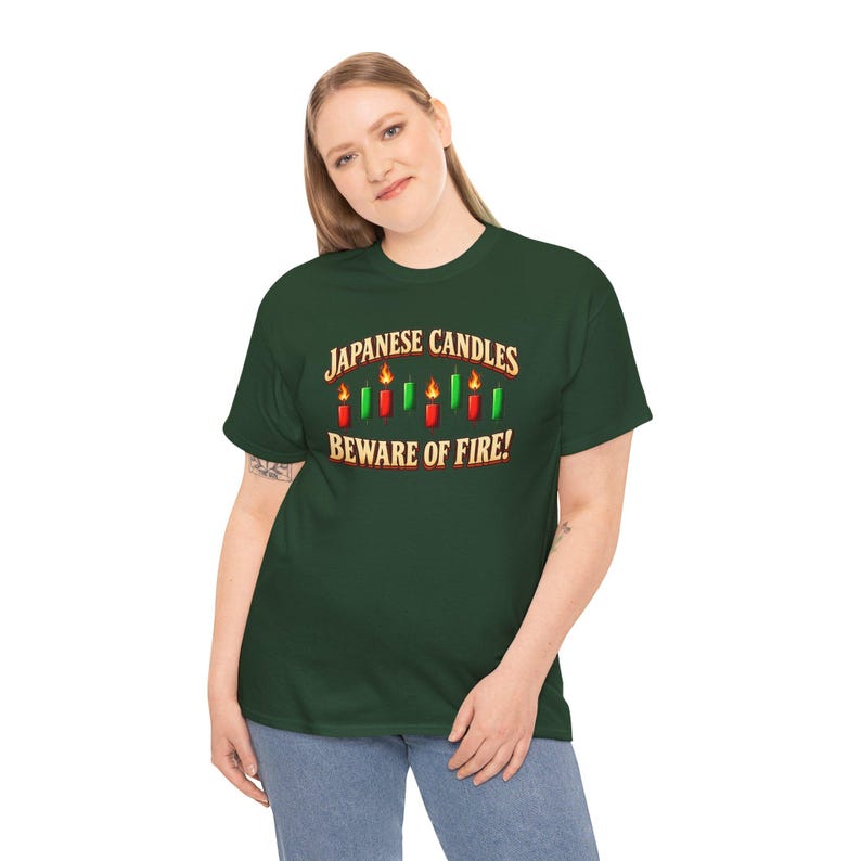 May include: A dark green short-sleeve t-shirt featuring a graphic of red and green candles with flames. The text reads "JAPANESE CANDLES" above the candles and "BEWARE OF FIRE!" below them in a bold, light-coloured, serif font.