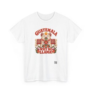 Puede incluir: Una camiseta blanca con un estampado gr&aacute;fico de dos llamas frente a frente, rodeadas de motivos florales rojos y verdes y un sol amarillo. El texto GUATEMALA aparece arqueado arriba y WHY NO LLAMA? est&aacute; impreso debajo de las llamas.