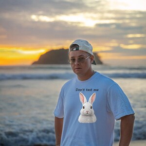 May include: A light blue short-sleeved t-shirt featuring a graphic of a white rabbit centered on the chest. Above the rabbit, the text "Don't test me" is printed in a simple black font. The shirt has a crew neckline and a relaxed fit.