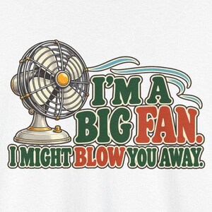 May include: A graphic print featuring a vintage-style electric fan with a yellow center. The text reads, I'M A BIG FAN. I MIGHT BLOW YOU AWAY. The lettering is in dark green and red with light blue swooshes representing air movement.
