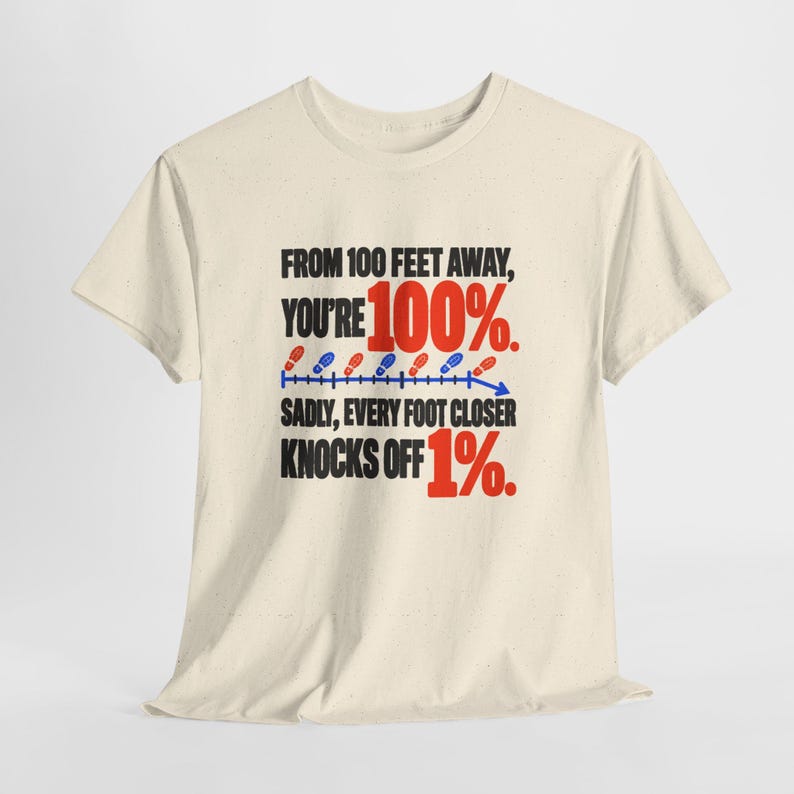 May include: A cream-colored short-sleeve t-shirt featuring black text that reads: FROM 100 FEET AWAY, YOU'RE 100%. SADLY, EVERY FOOT CLOSER KNOCKS OFF 1%. A blue line with red and blue shoe print icons illustrates a downward trend.