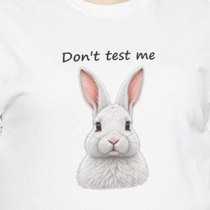 May include: A white t-shirt featuring a graphic of a fluffy white rabbit with pink-tinted ears. Above the rabbit, the text "Don't test me" is printed in a simple black sans-serif font. The design is centered on the front of the garment.