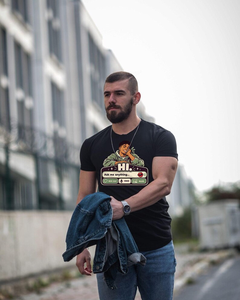 May include: A black short-sleeved t-shirt featuring a graphic print of a person in a green hoodie resting their chin on their hand. Below the figure is a chat interface box with the text "HI." and "Ask me anything..." along with icons.