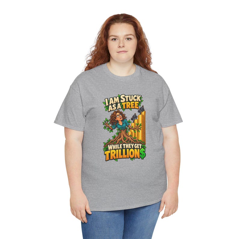 May include: A heather gray short-sleeve t-shirt featuring a graphic of a person with brown hair emerging from a tree trunk. The text reads I AM STUCK AS A TREE WHILE THEY GET TRILLION$ above and below the illustration with gold coins.