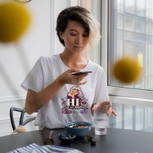 May include: A white short-sleeved t-shirt featuring a graphic print of a woman with long gray hair, glasses, and a purple top. The text reads HI Ask me anything, with icons for New Chat, Voice, and Image below the main text.