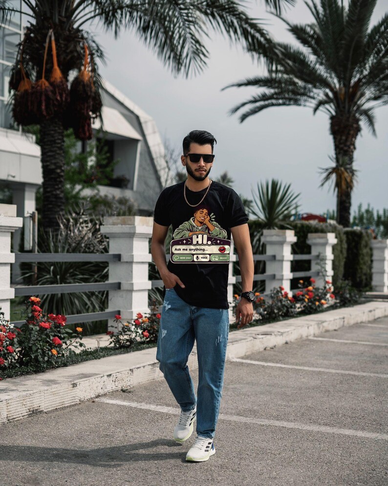 May include: A black short-sleeve t-shirt featuring a graphic of a person resting their chin on their hand with the text HI. Ask me anything... and icons for voice and message, paired with blue denim jeans and white athletic sneakers.