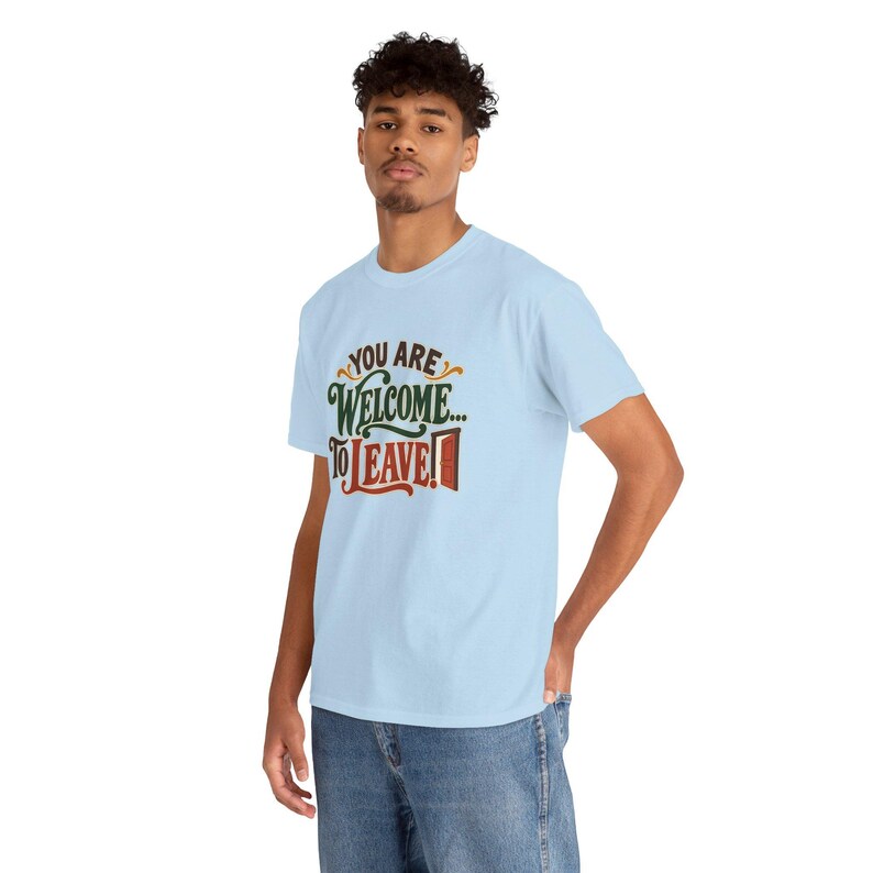 May include: A light blue short-sleeve t-shirt featuring the text "YOU ARE WELCOME... TO LEAVE!" printed on the chest. The word "WELCOME" is in dark green, while "TO LEAVE!" is in red with a small graphic of an open door.