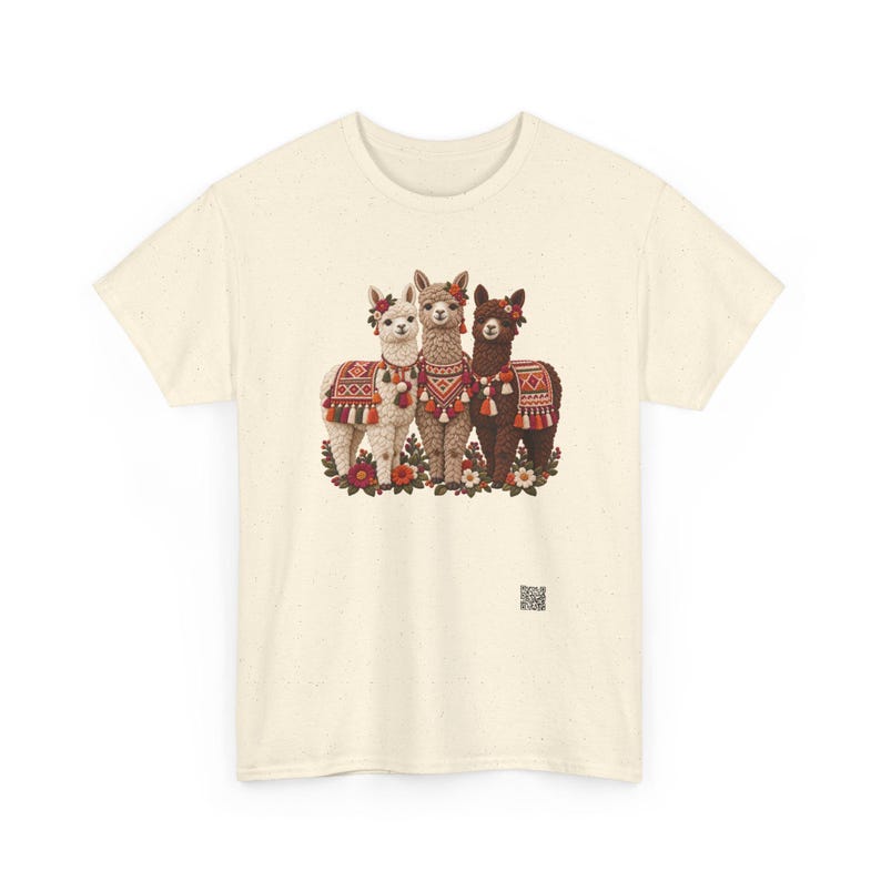 May include: A cream-colored short-sleeve t-shirt featuring a graphic of three llamas in white, tan, and dark brown. Each llama wears a colorful patterned blanket, tassels, and floral headpieces. A small QR code is printed near the bottom right.