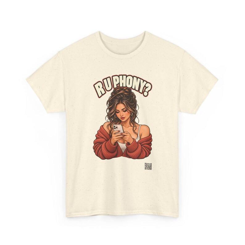 May include: A cream-colored short-sleeve t-shirt featuring a graphic illustration of a person with long brown hair wearing a red cardigan and looking at a smartphone. The text "RU PHONY?" is printed in brown above the illustration.