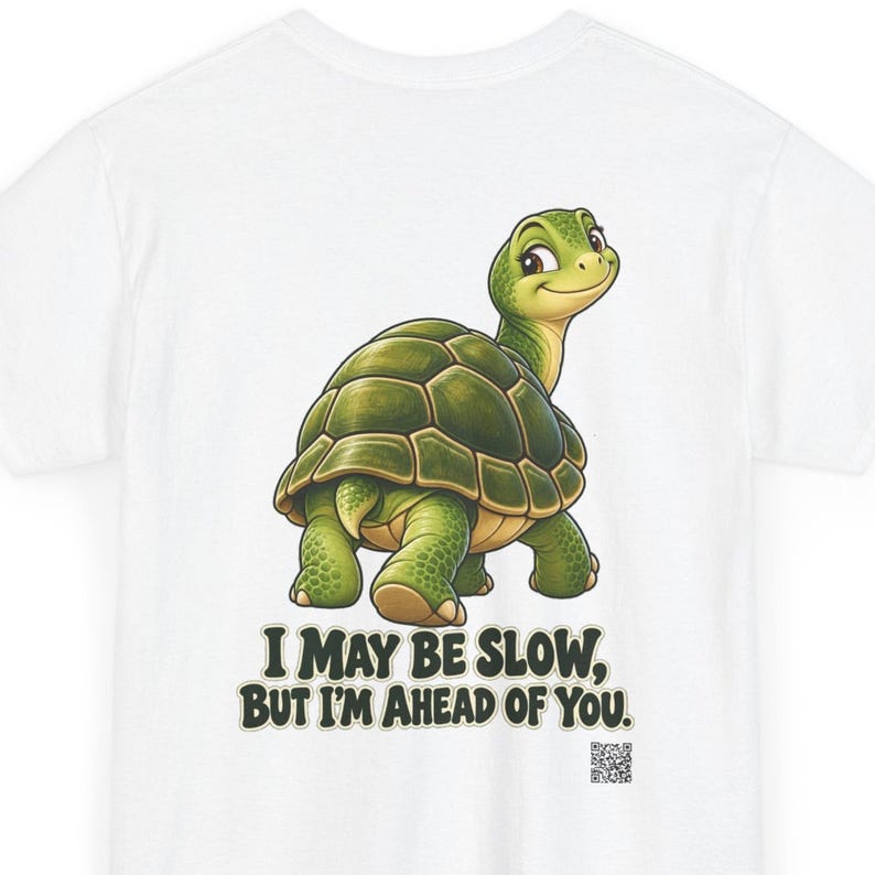 May include: A white t-shirt featuring a cartoon green turtle looking back over its shoulder. Below the turtle, the text reads, "I MAY BE SLOW, BUT I'M AHEAD OF YOU." A small QR code is printed in the bottom right corner of the graphic design.