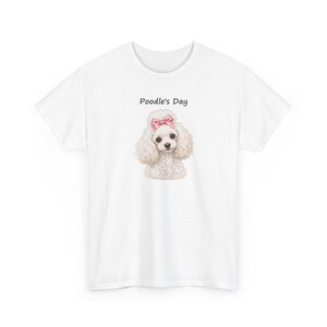 May include: A white short-sleeved t-shirt featuring a centered graphic of a fluffy white poodle with a pink bow on its head. Above the poodle, the text Poodle's Day is printed in a simple black font. The shirt has a crew neckline.