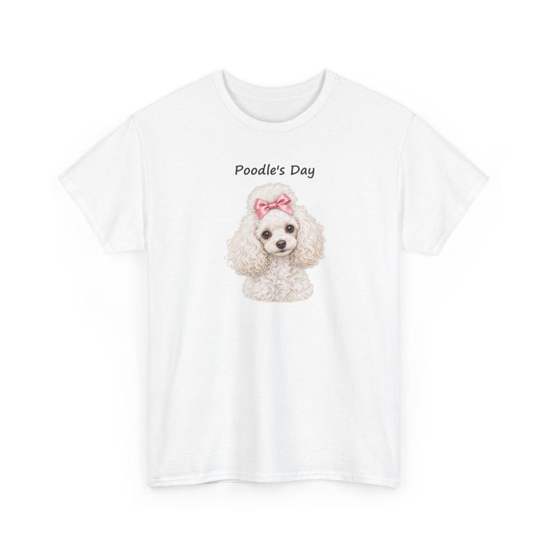 May include: A white short-sleeved t-shirt featuring a centered graphic of a fluffy white poodle with a pink bow on its head. Above the poodle, the text Poodle's Day is printed in a simple black font. The shirt has a crew neckline.
