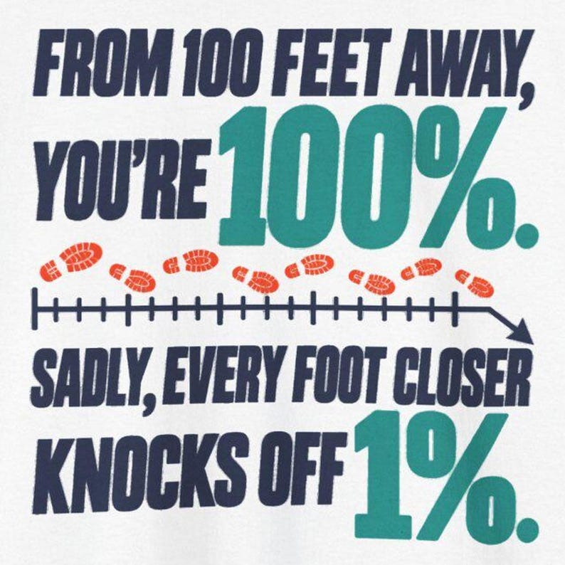 May include: A white graphic t-shirt featuring dark blue and teal text that reads: FROM 100 FEET AWAY, YOU'RE 100%. SADLY, EVERY FOOT CLOSER KNOCKS OFF 1%. Between the text lines is a horizontal measurement line with orange footprints.