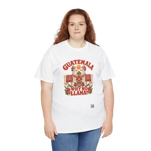 Puede incluir: Una camiseta blanca de manga corta con un gr&aacute;fico de dos llamas frente a frente, rodeadas de flores y un sol. El texto GUATEMALA WHY NO LLAMA? aparece en letras rojas. Un peque&ntilde;o c&oacute;digo QR cuadrado est&aacute; impreso bajo el dise&ntilde;o.