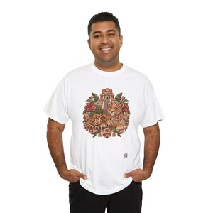 May include: A white short-sleeve t-shirt featuring a central graphic of a spotted jaguar resting in front of a stepped pyramid, surrounded by red hibiscus flowers and geometric patterns in shades of brown, orange, and green.