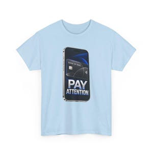 May include: A light blue t-shirt featuring a graphic of a smartphone displaying a black credit card labeled BANK OF MINE and the text PAY ATTENTION in bold white letters. The design is centered on the chest of the short-sleeved garment.