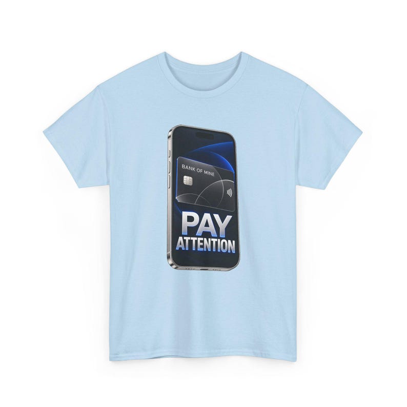 May include: A light blue t-shirt featuring a graphic of a smartphone displaying a black credit card labeled BANK OF MINE and the text PAY ATTENTION in bold white letters. The design is centered on the chest of the short-sleeved garment.