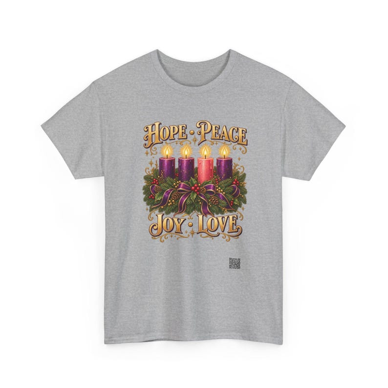 May include: A heather gray t-shirt featuring a graphic of four lit candles nestled in a green wreath with purple ribbons. The text above reads HOPE PEACE and the text below reads JOY LOVE in a gold font. A small QR code is visible at the bottom.