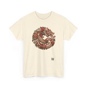 Puede incluir: Una camiseta de manga corta color crema con un gr&aacute;fico circular de una serpiente estilizada entrelazada con elementos florales en tonos rojos, naranjas, marrones y verdes. Un peque&ntilde;o c&oacute;digo QR cuadrado est&aacute; impreso cerca del dobladillo inferior derecho.