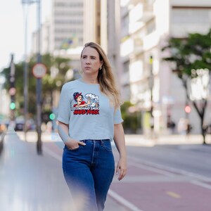 May include: A light blue short-sleeve t-shirt featuring a graphic print of a person with a red headband waving a hand in front of smoke. The text below the graphic reads SECONDHAND SMOKE HARD PASS in bold black and red capital letters.