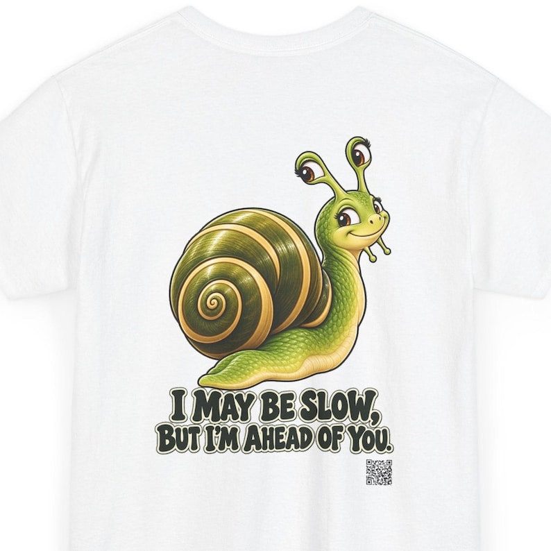 May include: A white t-shirt featuring a cartoon snail with a green body and a dark green spiral shell. Below the snail, the text reads, "I MAY BE SLOW, BUT I'M AHEAD OF YOU." A small QR code is printed in the bottom right corner of the graphic.