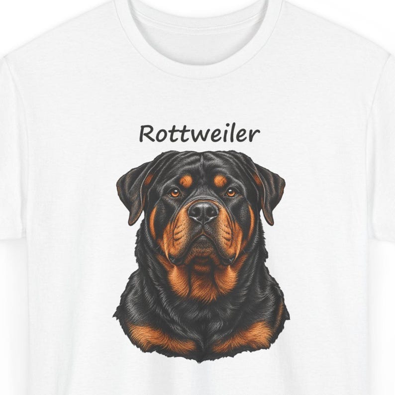 May include: A white t-shirt featuring a detailed illustration of a Rottweiler dog head centered on the chest. Above the dog, the word Rottweiler is printed in a simple black sans-serif font. The dog has black and tan fur.
