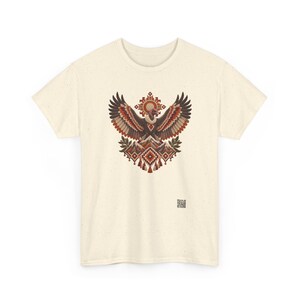 May include: A cream-colored short-sleeve t-shirt featuring a central graphic of a vulture with wings spread wide above stylized mountains and geometric patterns in shades of brown, orange, and red. A small QR code is printed near the bottom right.