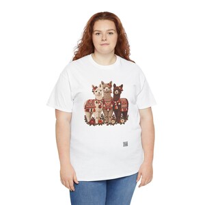 May include: A white t-shirt featuring a graphic print of three alpacas standing together. The alpacas are adorned with colorful patterned blankets, tassels, and floral headpieces. The design includes red, brown, and cream tones.
