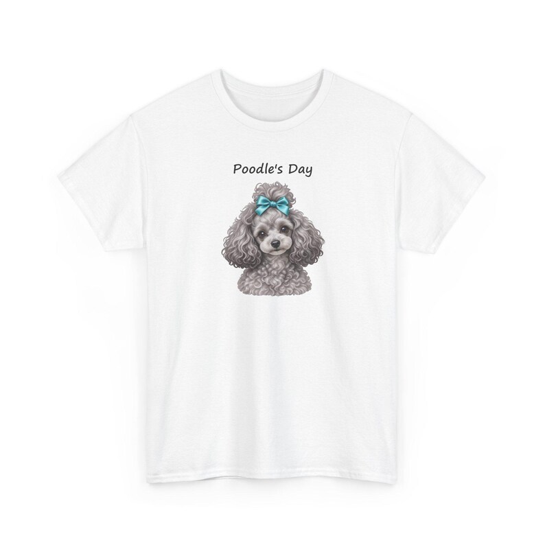 Puede incluir: Una camiseta blanca de manga corta con el gr&aacute;fico de un caniche gris con un lazo azul brillante en la cabeza. Sobre el caniche, el texto Poodle's Day est&aacute; impreso en una fuente negra sencilla. La camiseta tiene cuello redondo y corte est&aacute;ndar.